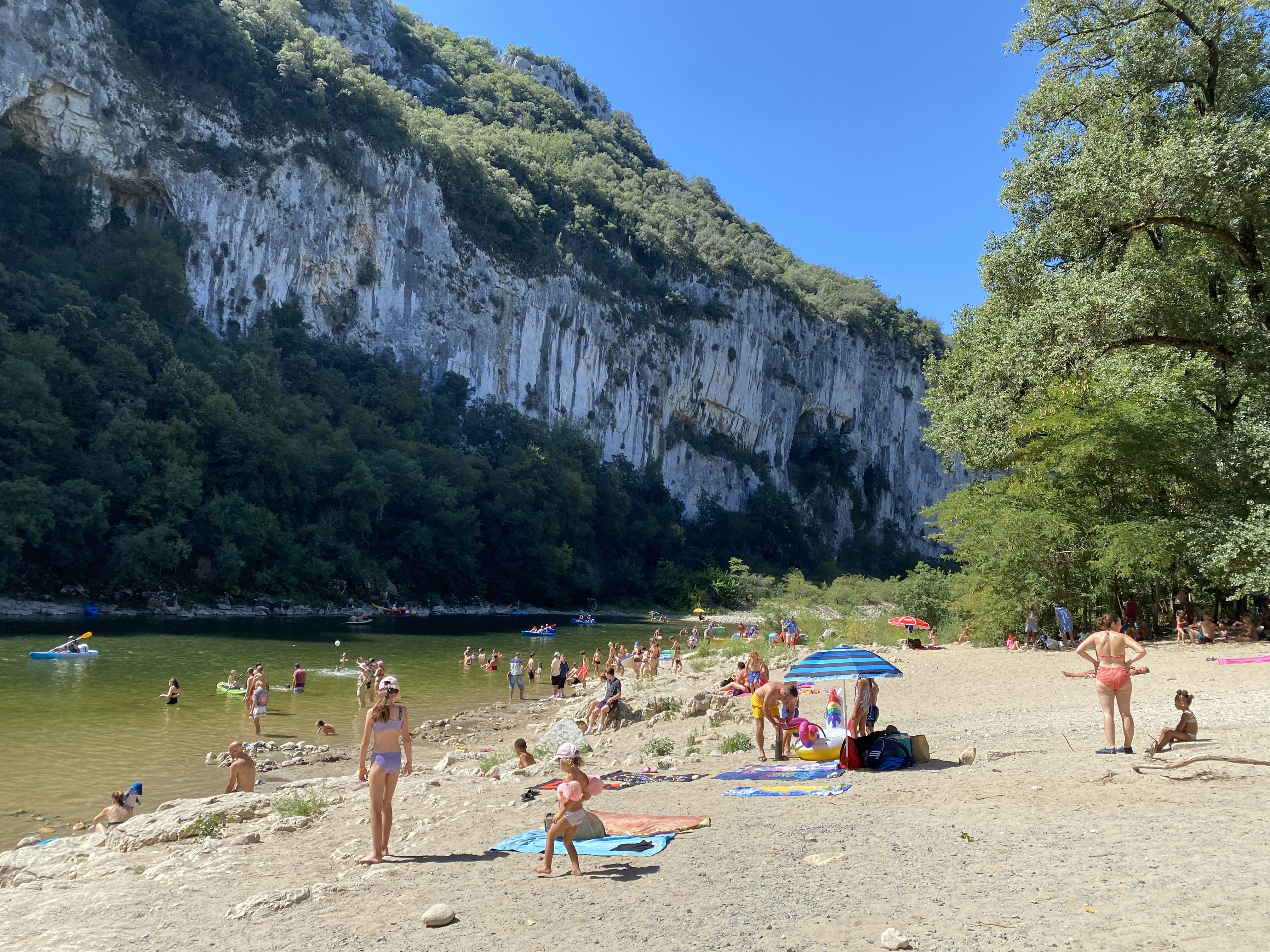 Druk bezocht kiezelstrand aan de voet van hoge kalkstenen kliffen bij de Pont d'Arc