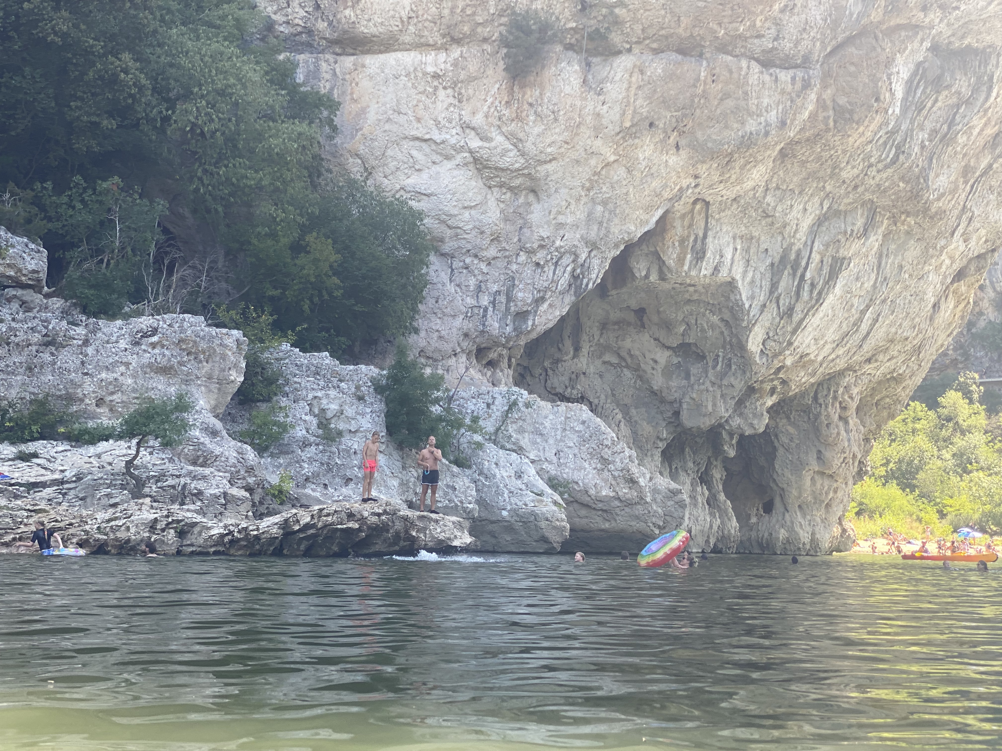 Mensen staan op rotsen bij de Pont d'Arc met uitzicht op het groene water van de Ardèche